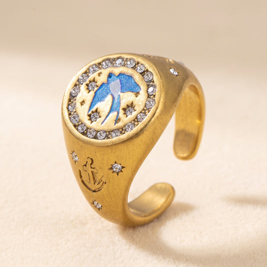 Homeward Swallow signet ring in brushed gold, a painted blue swallow framed by clear stones